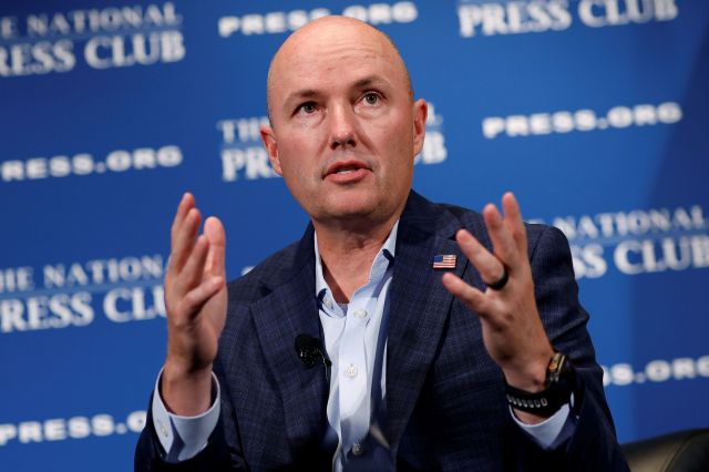 Gov. Spencer Cox in a blazer gestures while speaking at a podium with a blue backdrop featuring the National Press Club logo.