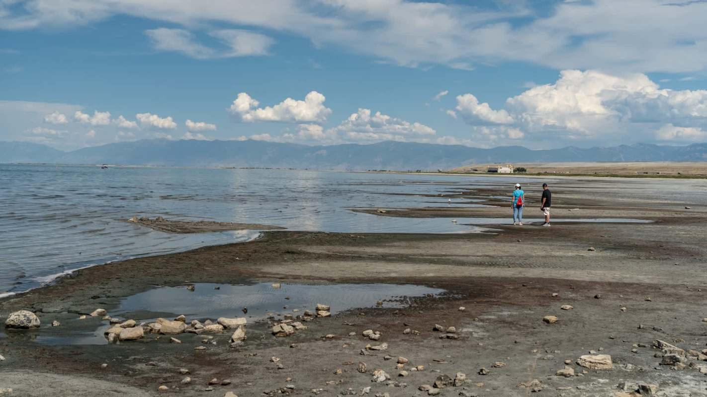 Two people walk along a beach at Great Salt Lake in Utah with receding water.
