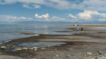 Two people walk along a beach at Great Salt Lake in Utah with receding water.