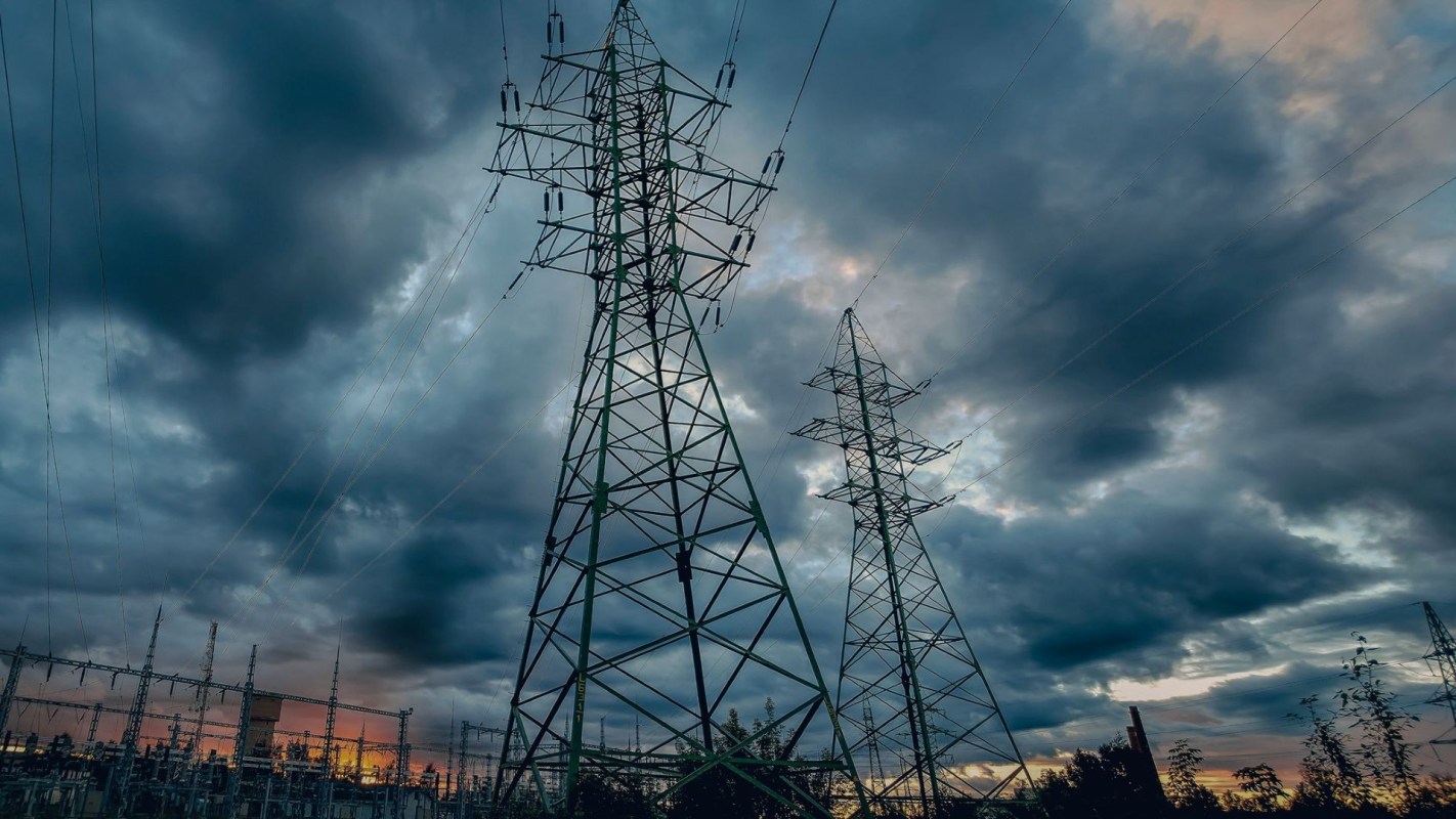 Two tall power transmission towers stand against a cloudy sky at sunset, with electrical cables running between them.