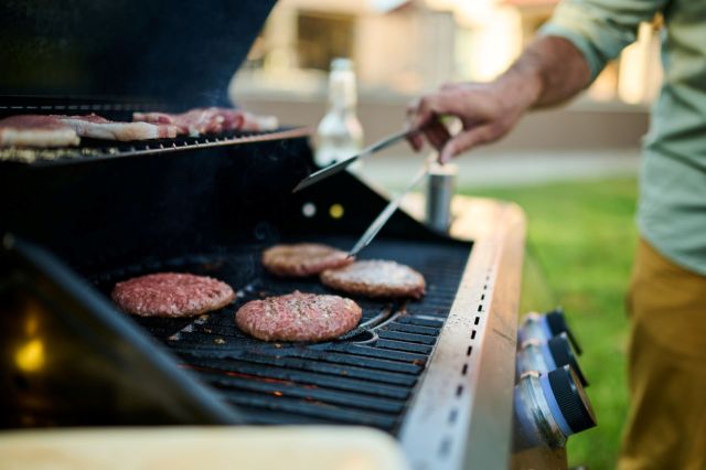 A person is grilling hamburger patties on an outdoor barbecue in a backyard setting.