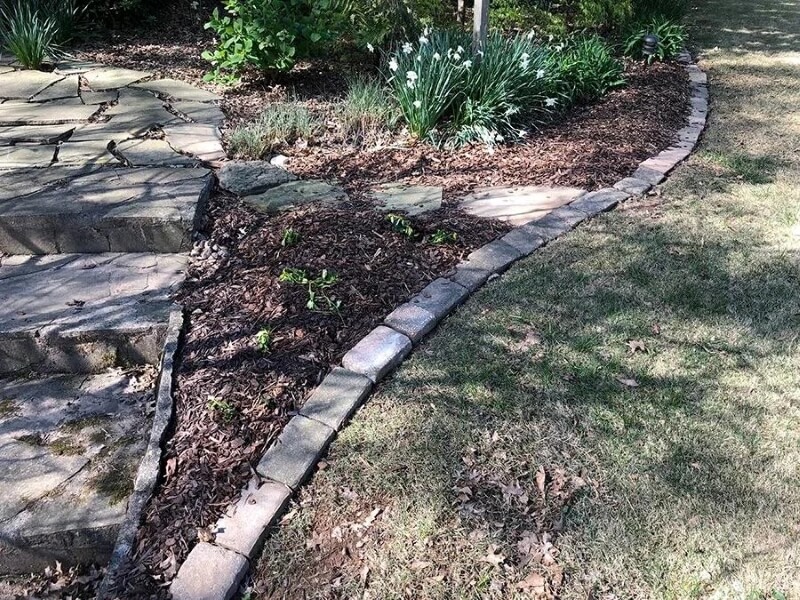 A stone border between a lawn and a plant bed next to a garden path.