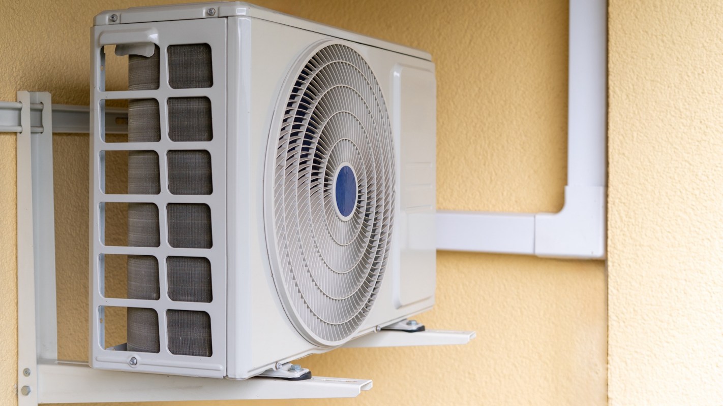 An air conditioning unit with visible piping mounted to a yellow wall.