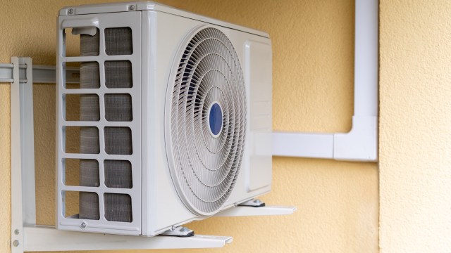 An air conditioning unit with visible piping mounted to a yellow wall.
