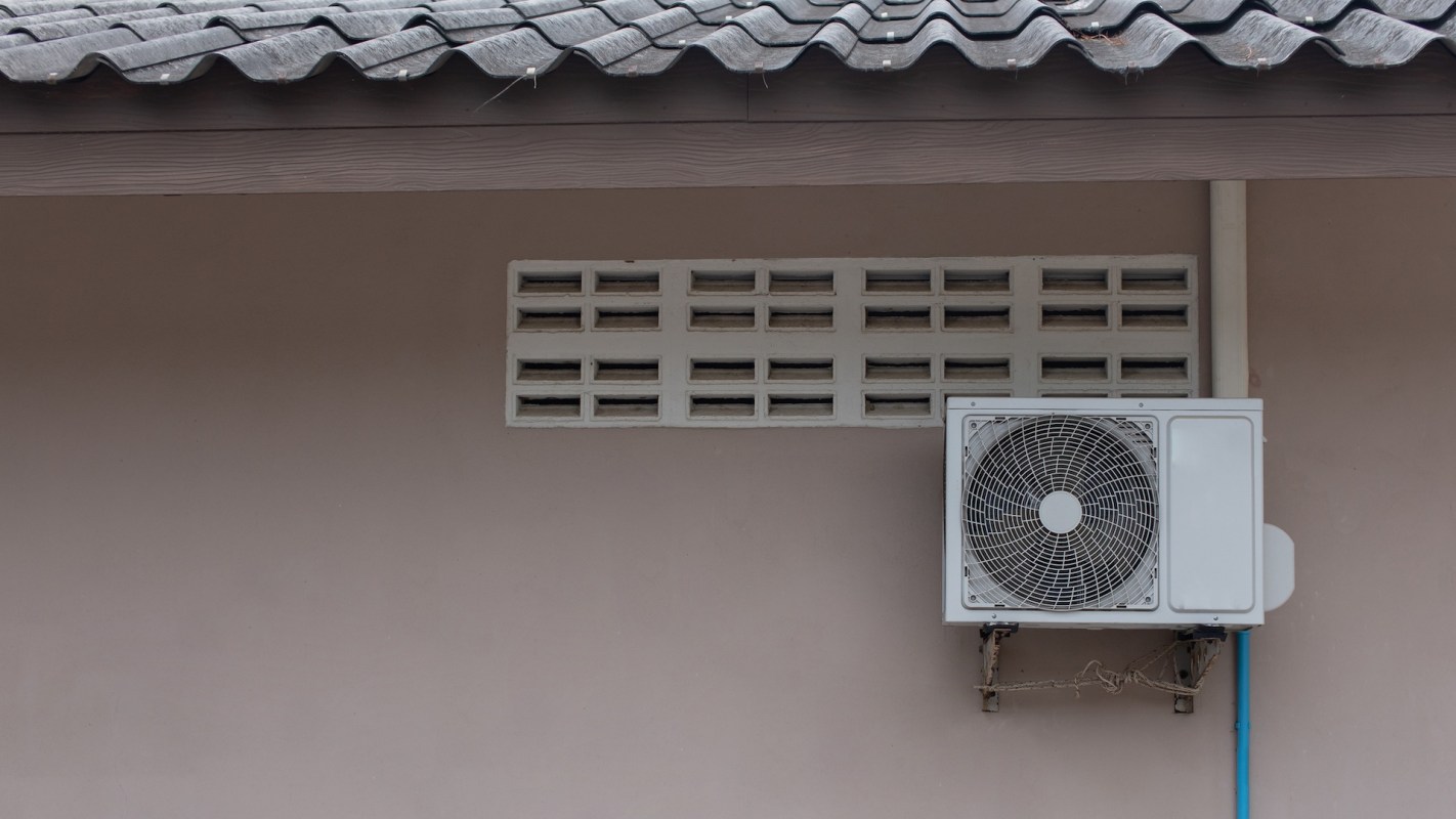 An exterior wall featuring a white air conditioning unit and a decorative vent above it.