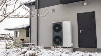 An outdoor heat pump unit beside a dark door, set against a snowy landscape.