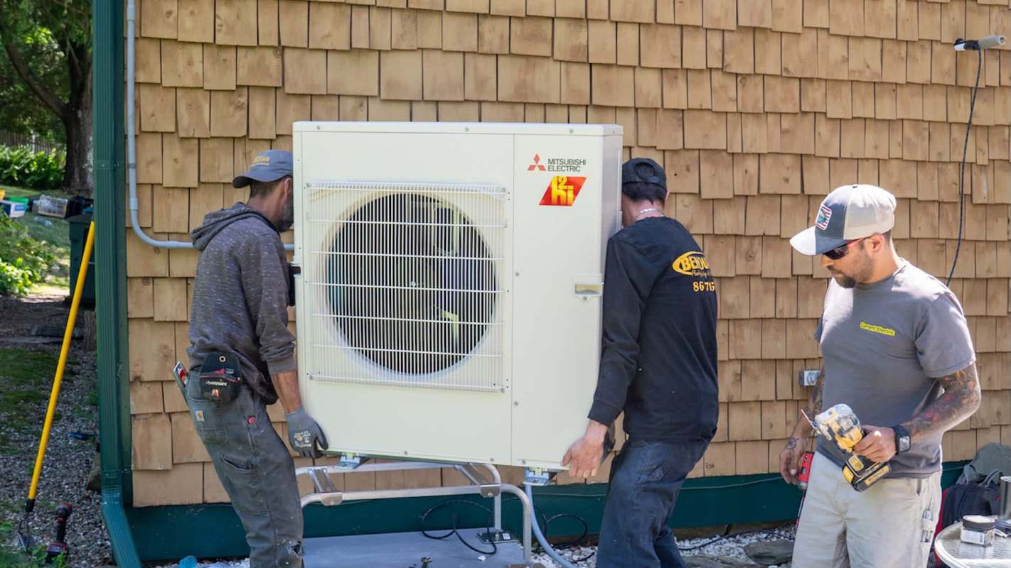 Three technicians are installing a Mitsubishi heat pump by a wooden shingle wall.