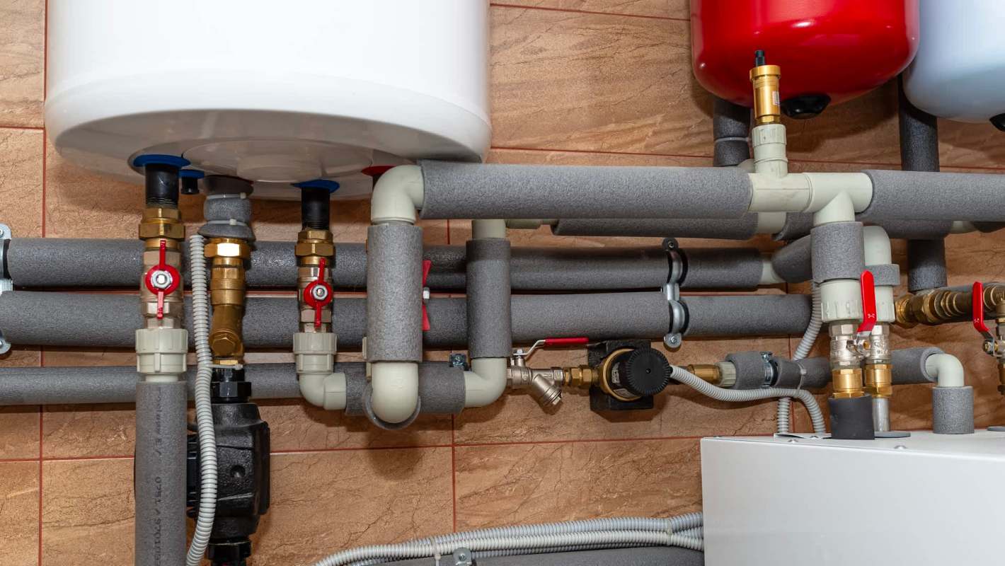 A complex arrangement of pipes and valves connected to water heaters in a residential utility room.