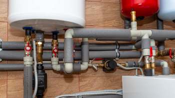 A complex arrangement of pipes and valves connected to water heaters in a residential utility room.