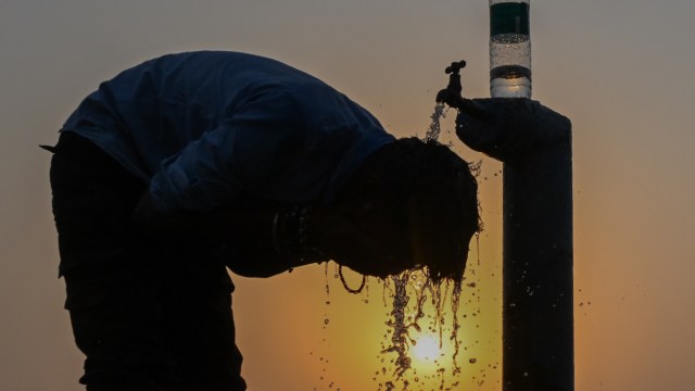 A person leans over a water tap, washing their hair at sunset.