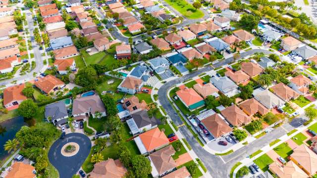 An aerial view of a suburban neighborhood featuring houses, gardens, and winding roads.