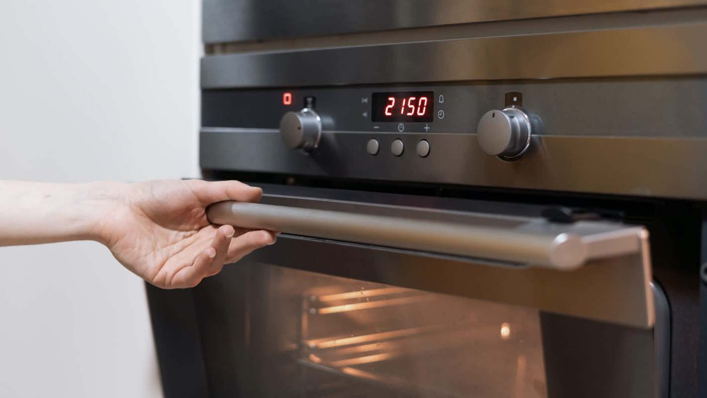 A hand is opening the oven door, revealing the inside illuminated by the oven light.