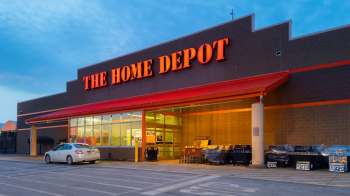 A Home Depot store entrance with carts outside and various grills displayed along the side.