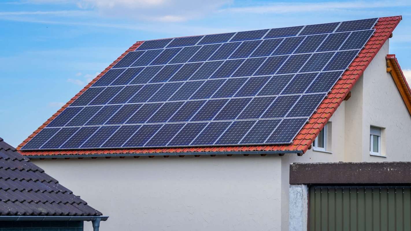 A house with a red-tiled roof featuring solar panels under a blue sky.