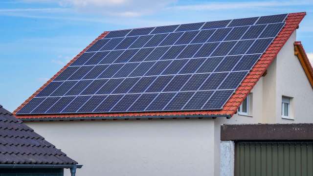 A house with a red-tiled roof featuring solar panels under a blue sky.