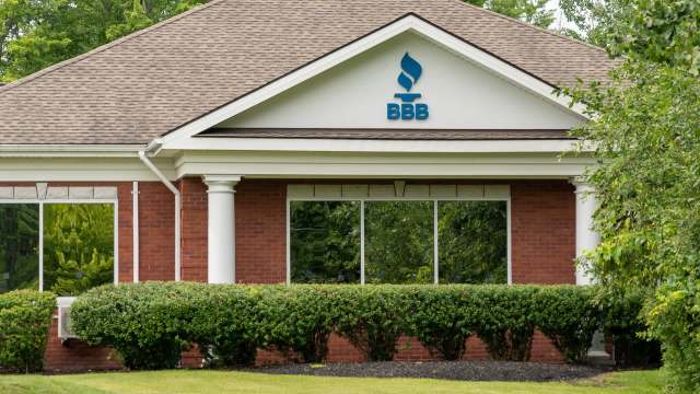 A brick building featuring a "BBB" sign for the Better Business Bureau, surrounded by lush green bushes and trees.