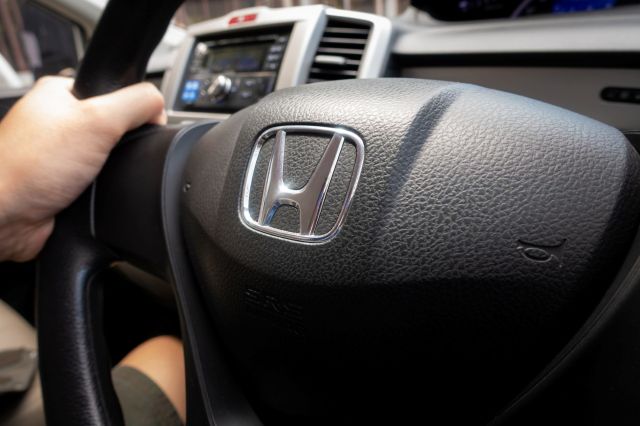 A close-up of a hand gripping a Honda steering wheel with the logo prominently displayed.