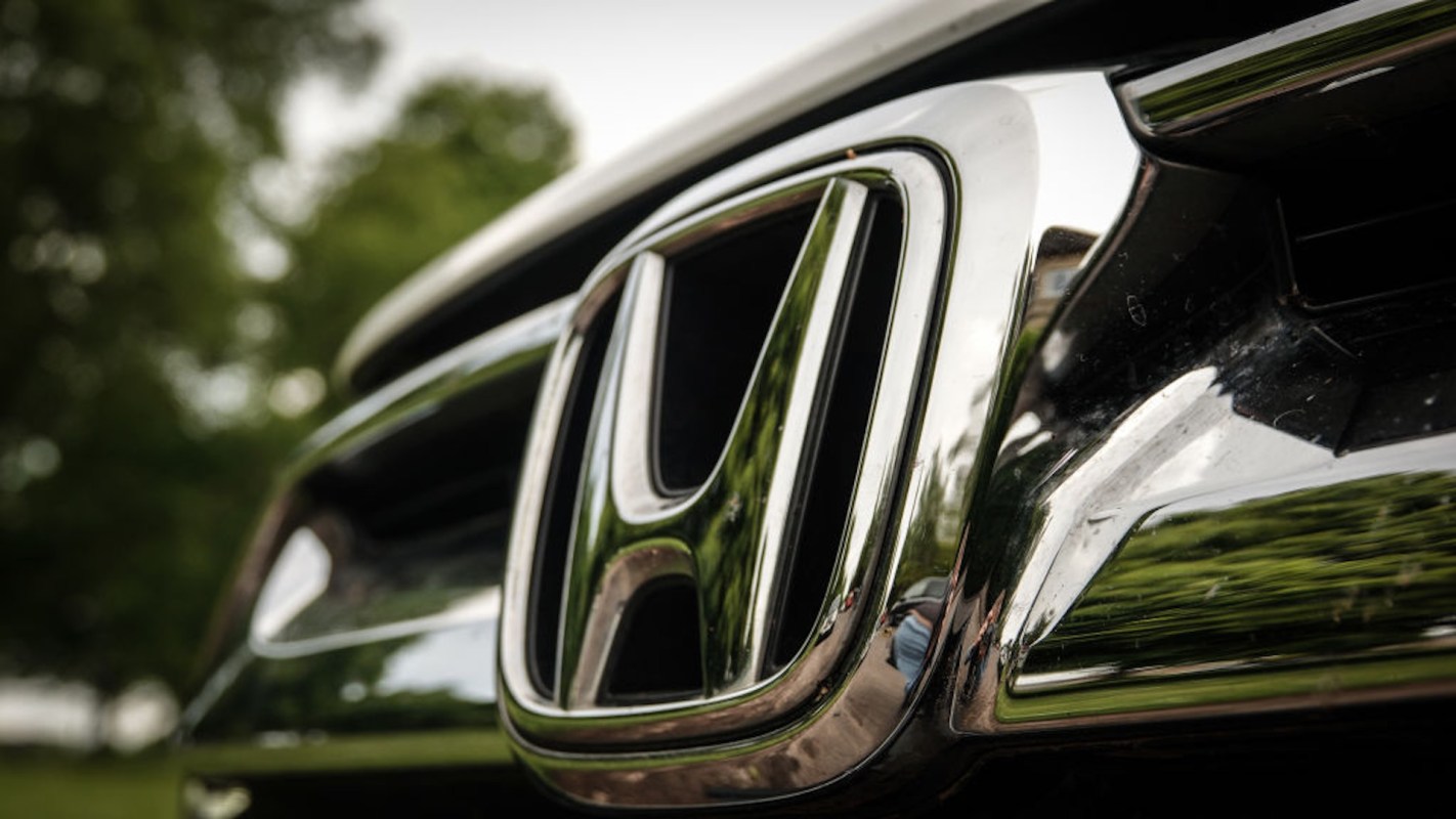 Close-up of a shiny Honda emblem on a car with greenery blurred in the background.