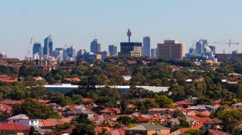 A panoramic view of a city skyline in Sydney, Australia, with modern buildings and greenery in the foreground.