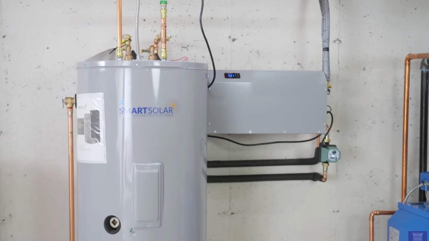 A gray SmartSolar heat pump water heater connected to copper pipes against a concrete wall.