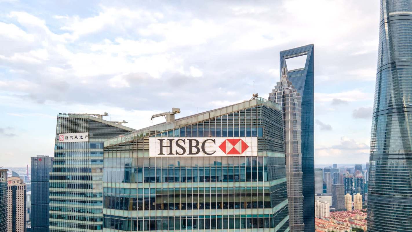 A high-rise building with an HSBC logo, surrounded by modern skyscrapers under a partly cloudy sky.
