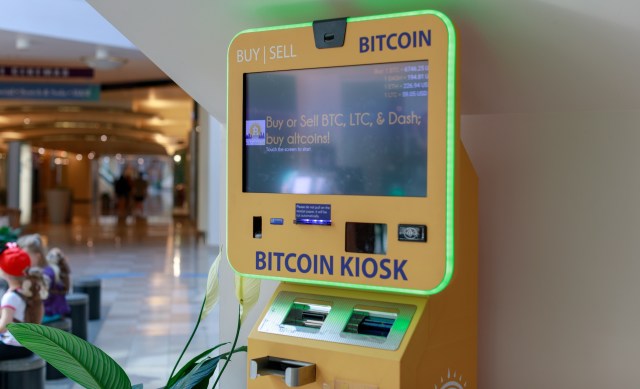 A brightly lit bitcoin kiosk displaying cryptocurrency options in a modern indoor setting.