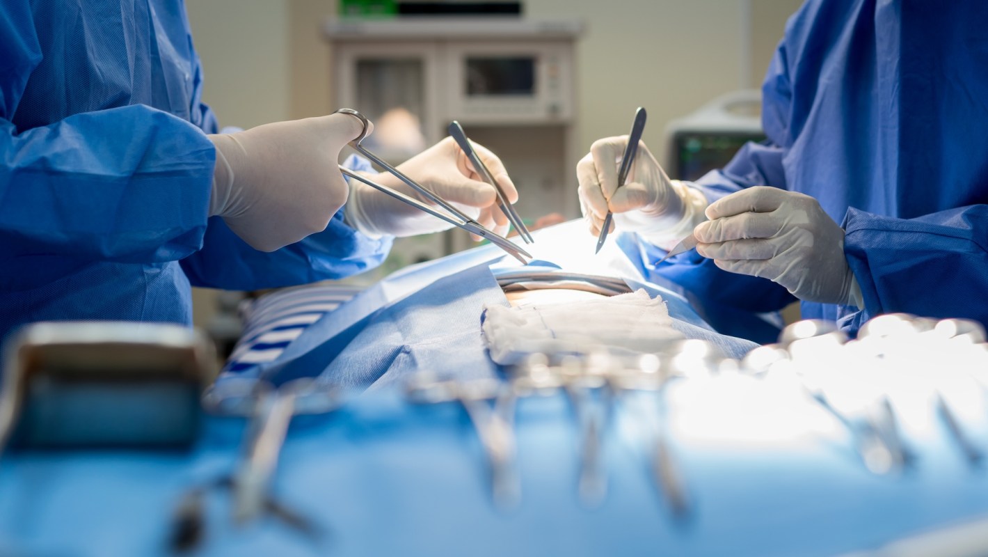 Medical professionals performing a surgery, focused on a patient covered with blue surgical drapes.