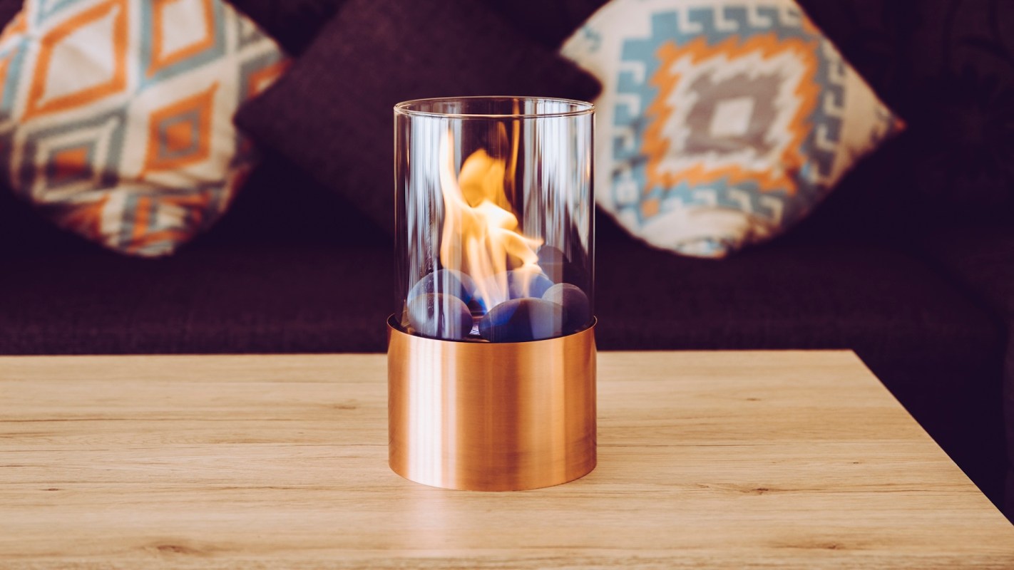 A decorative portable indoor fireplace with a glass enclosure and colorful stones, placed on a wooden table.