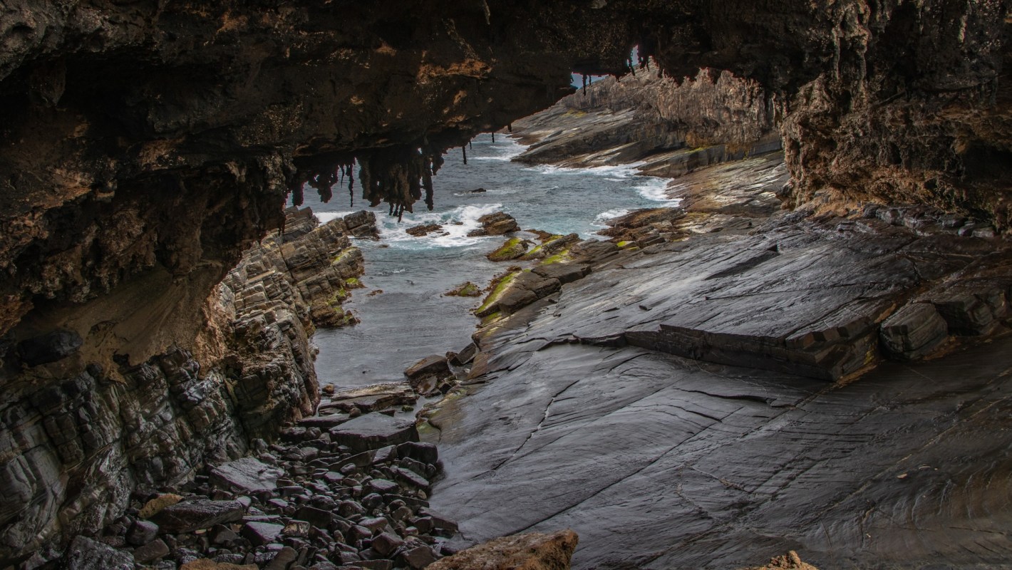 A rocky coastline viewed through a natural arch, with waves lapping against the shore.