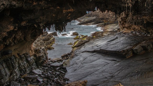 A rocky coastline viewed through a natural arch, with waves lapping against the shore.