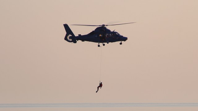 A helicopter hovers above water while a police officer is lowered on a rope.