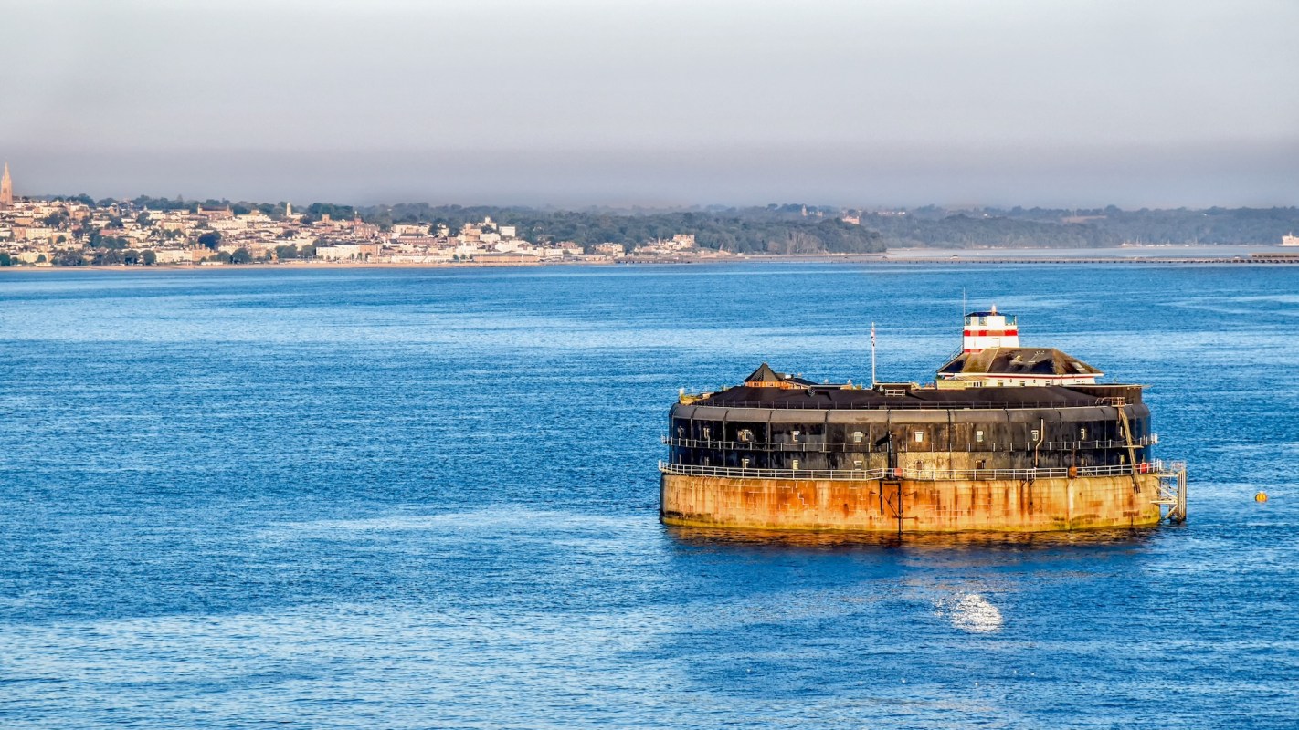 A circular fortification in a middle of water, with the shoreline in the distance.
