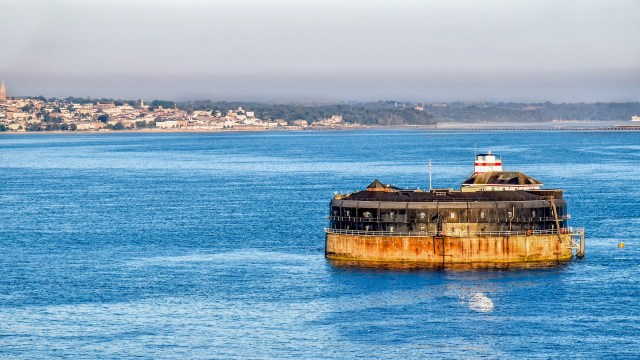 A circular fortification in a middle of water, with the shoreline in the distance.