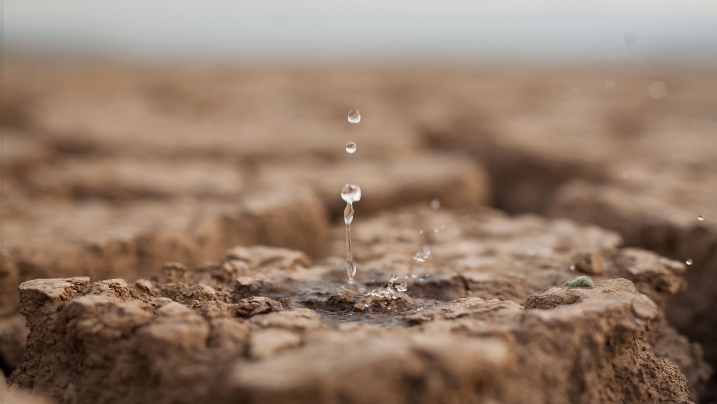 Water droplets rise from cracked, dry earth, illustrating drought conditions in a close-up view.