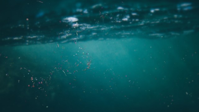 Colorful microplastic particles float underwater, with soft light filtering through the surface.