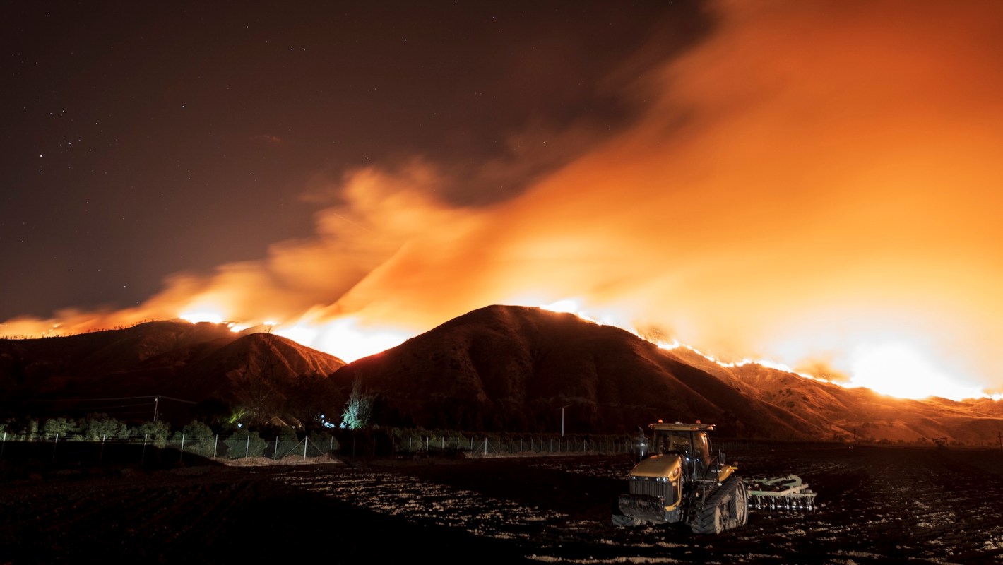 Smoke billows from a wildfire on a hillside at night.