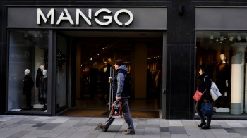 A man walks past a clothing store named "MANGO" with mannequins visible in the window displays.