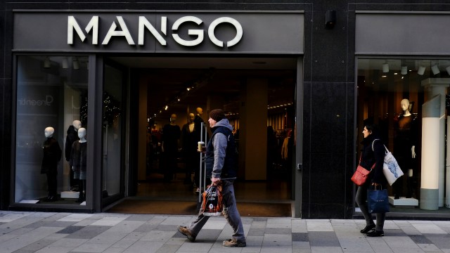 A man walks past a clothing store named "MANGO" with mannequins visible in the window displays.