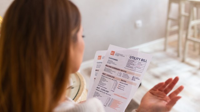 A woman expressed outrage with her right hand after reviewing her utility bill while sitting at a table in a well-lit room.