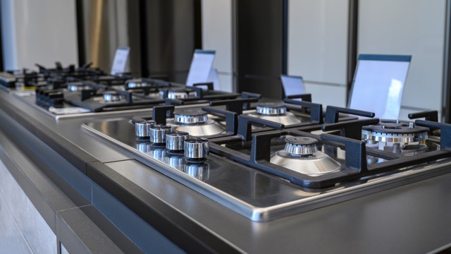A close-up of a modern gas cooktop in a retail store with multiple burners and sleek stainless steel and black components.