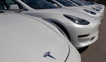 A row of white Tesla cars parked in a lot, showcasing their sleek designs and distinctive logo.