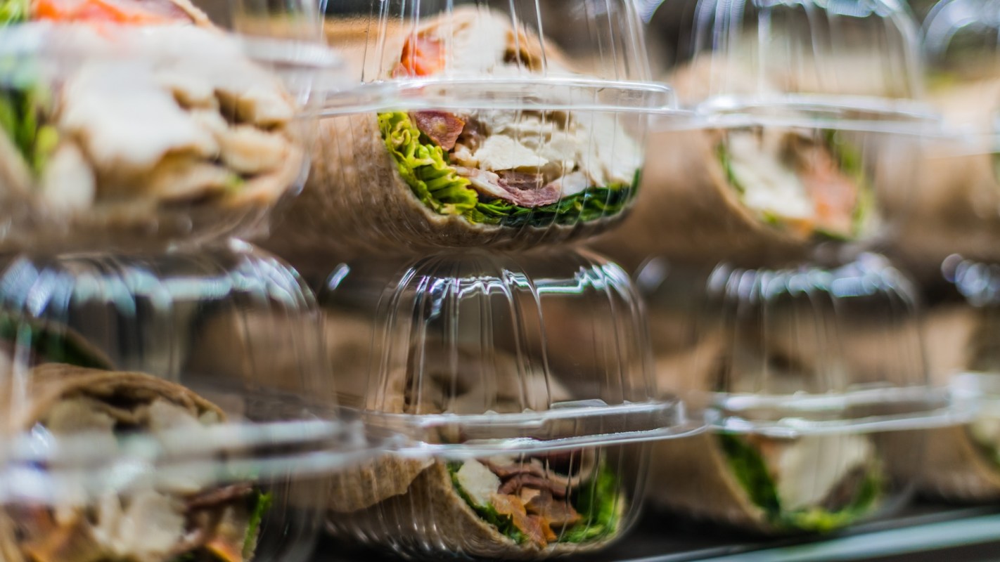 A close-up of wrapped sandwiches in clear plastic containers, featuring visible ingredients like lettuce and meat.