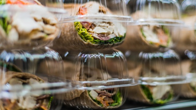 A close-up of wrapped sandwiches in clear plastic containers, featuring visible ingredients like lettuce and meat.
