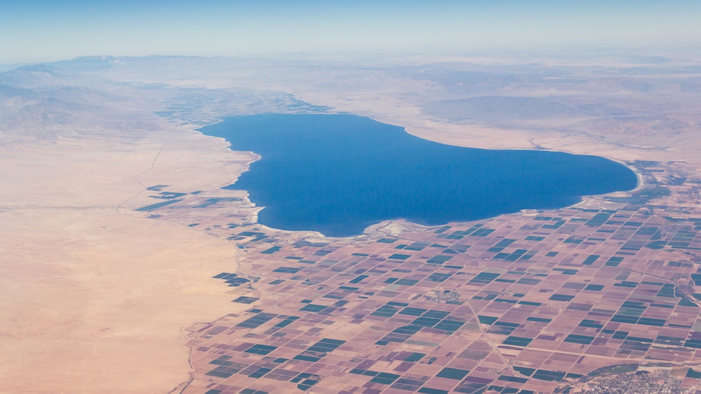 Aerial view of a large body of water surrounded by vast, patterned agricultural fields and desert terrain.