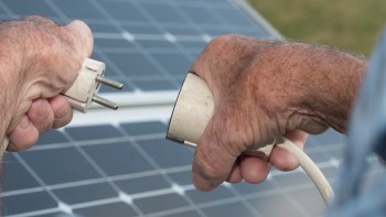 A close-up of hands connecting an electrical plug to a solar panel.