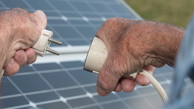 A close-up of hands connecting an electrical plug to a solar panel.