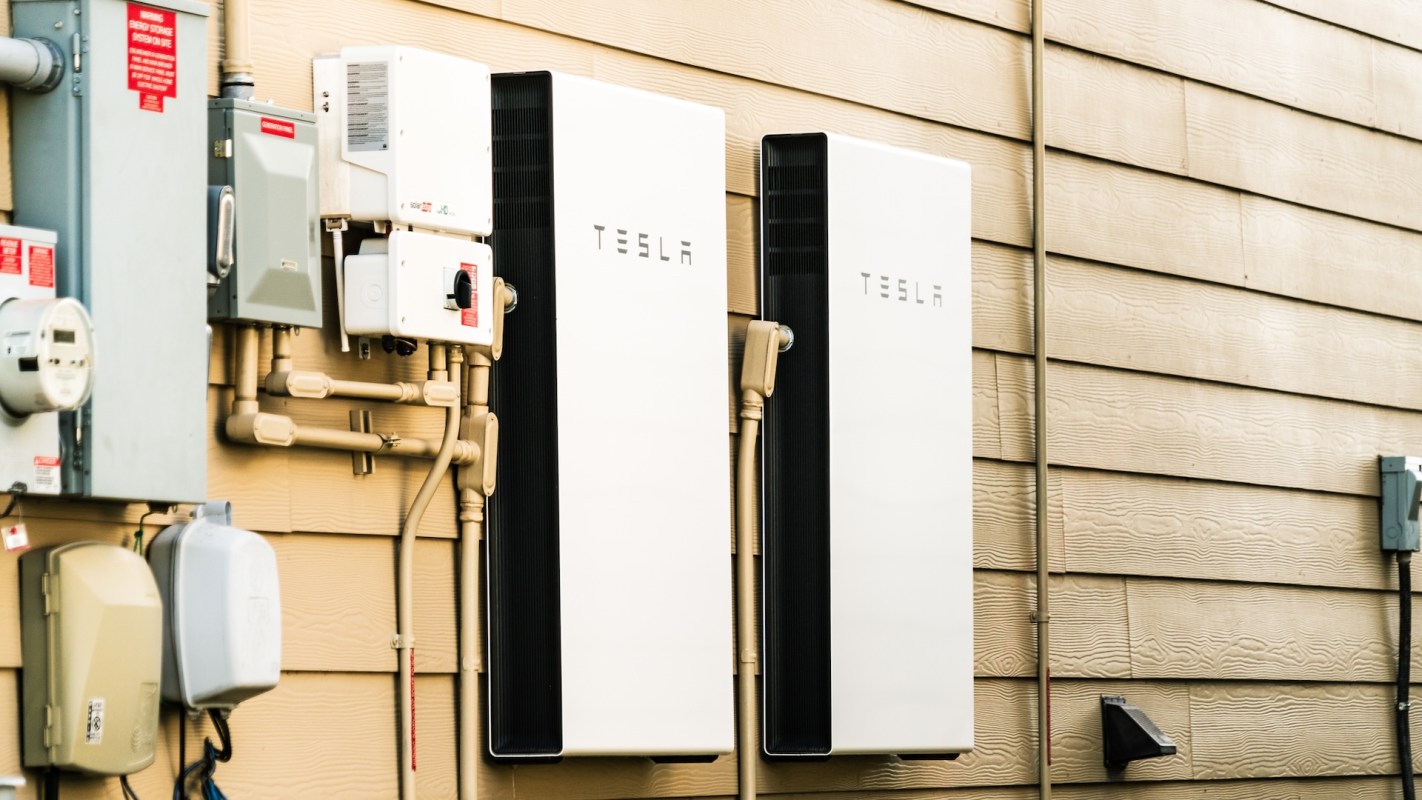 Two Tesla Powerwall energy storage units mounted on a wall next to electrical meters and control boxes.