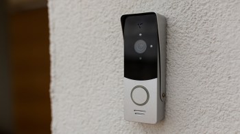 A modern video doorbell mounted on a textured white wall.