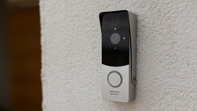 A modern video doorbell mounted on a textured white wall.