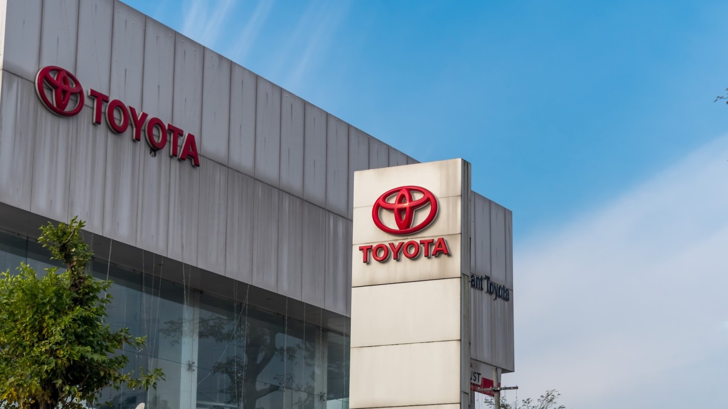 A Toyota dealership sign displayed outside a modern building against a clear blue sky.
